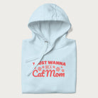 Graphic on a folded light blue hoodie saying 'I Just Wanna Be a Cat Mom' with pink lettering and paw prints.