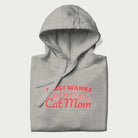 Graphic on a folded light grey hoodie saying 'I Just Wanna Be a Cat Mom' with pink lettering and paw prints.