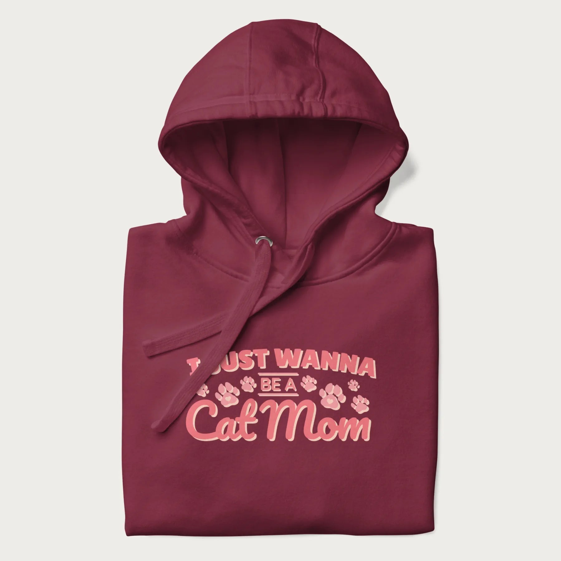 Graphic on a folded maroon hoodie saying 'I Just Wanna Be a Cat Mom' with pink lettering and paw prints.