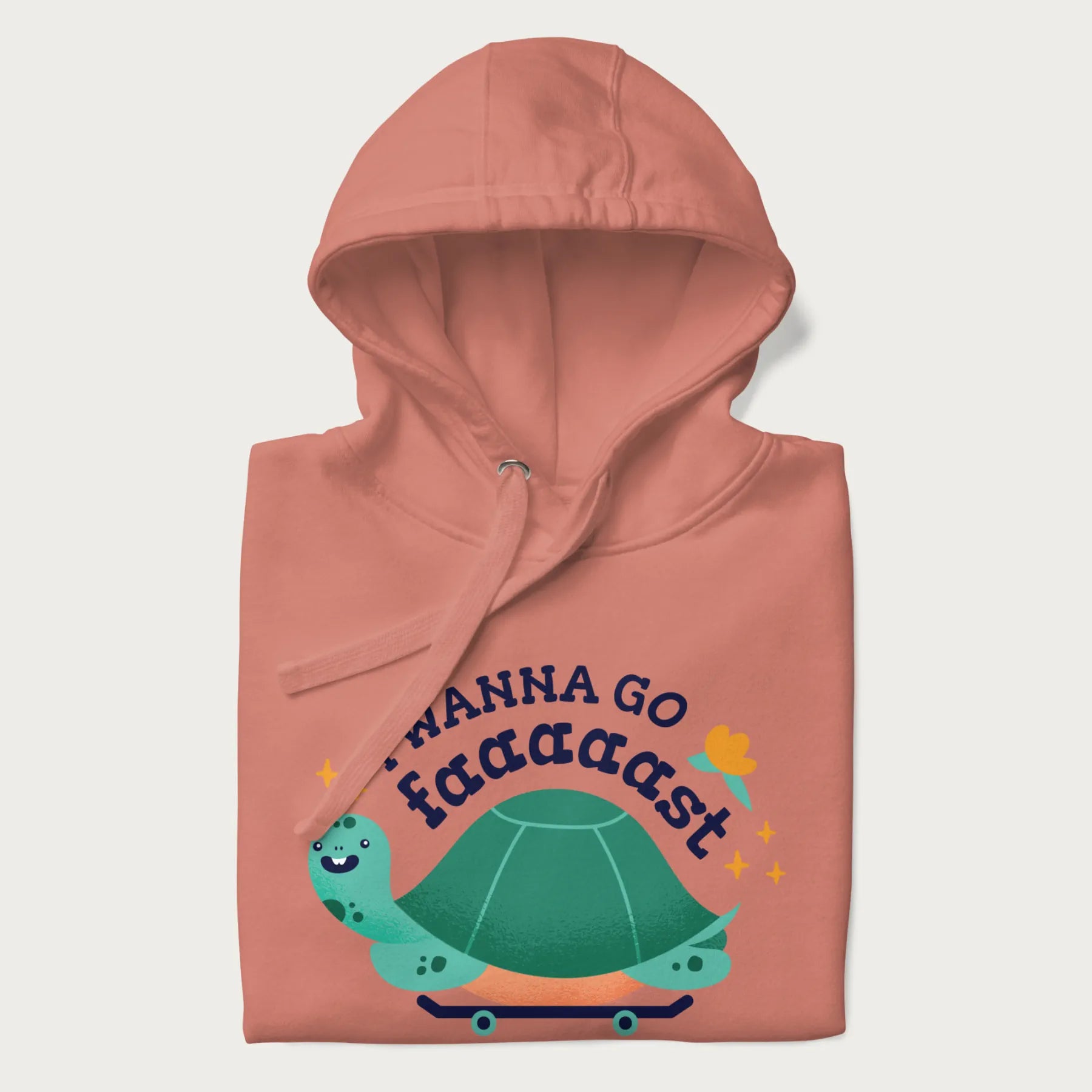 Folded light pink hoodie with a graphic of a happy turtle on a skateboard and the text 'I Wanna Go Faaaaast'.