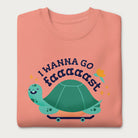 Folded light pink sweatshirt with a graphic of a turtle on a skateboard and the phrase 'I Wanna Go Fast.'