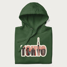 Folded forest green hoodie with graphic of Tokyo's skyline integrated into the word 'TOKYO' in sunset colors.