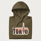 Folded military green hoodie with graphic of Tokyo's skyline integrated into the word 'TOKYO' in sunset colors.