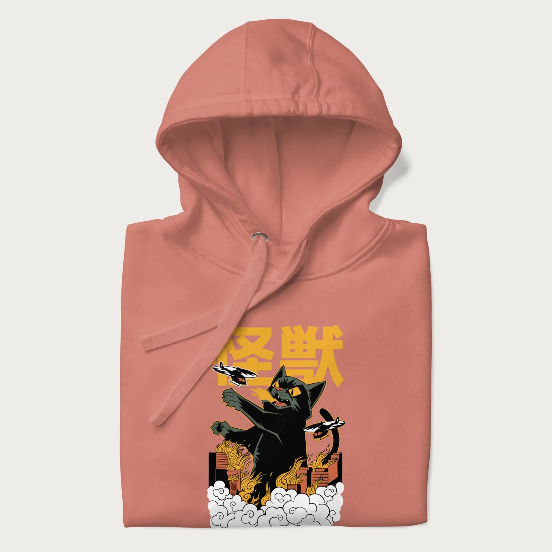Folded light pink hoodie with graphic of a 'Kaiju Cat' with helicopters and flames in a burning city.