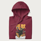 Folded maroon hoodie with graphic of a 'Kaiju Cat' with helicopters and flames in a burning city.