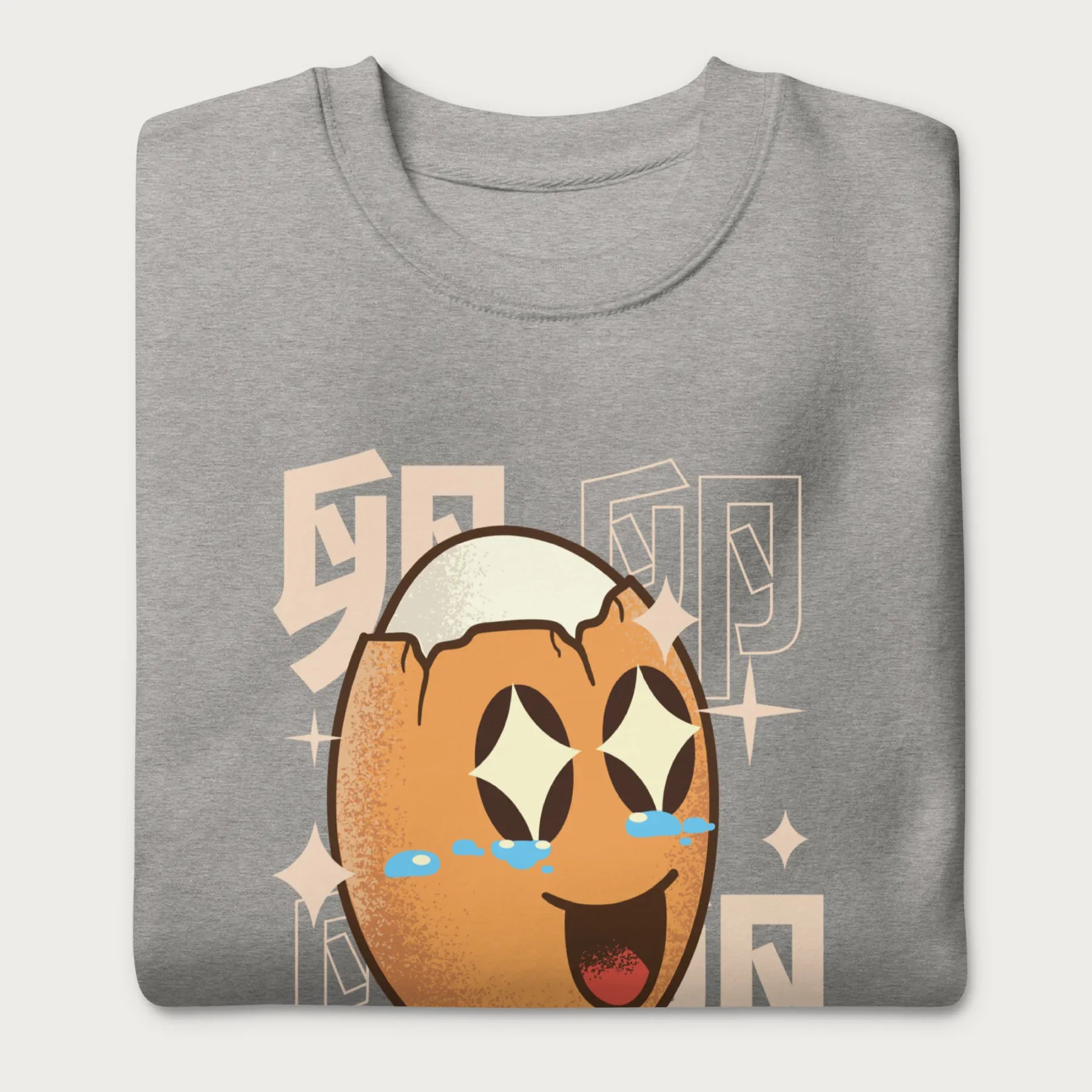 Folded light grey sweatshirt with Japanese text and a kawaii boiled egg graphic with sparkling eyes..