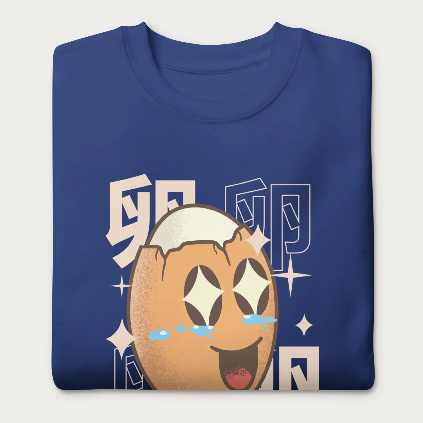 Folded royal blue sweatshirt with Japanese text and a kawaii boiled egg graphic with sparkling eyes..