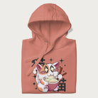 Folded light pink hoodie with Japanese graphic of a cat eating ramen with Japanese text '猫' in the background.