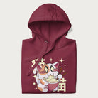 Folded maroon hoodie with Japanese graphic of a cat eating ramen with Japanese text '猫' in the background.