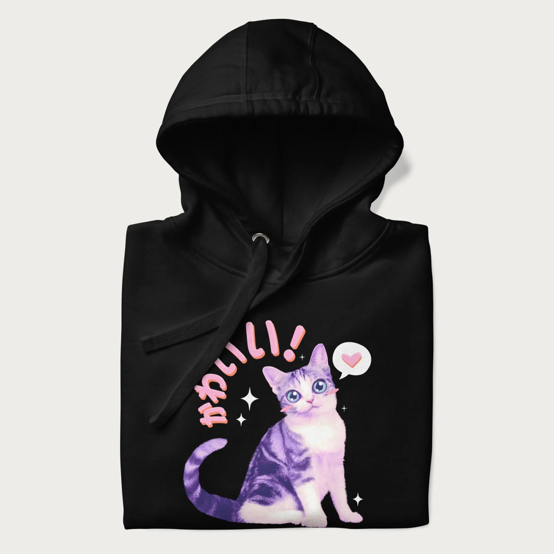 Folded black hoodie with a graphic of a blue-eyed kitten and Japanese kawaii-style lettering, stars, and a heart.