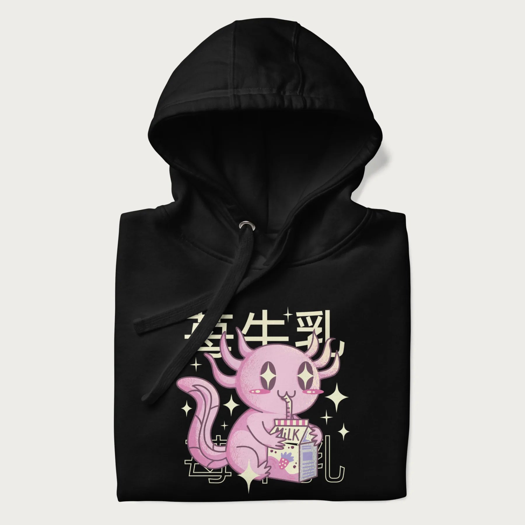 Folded black hoodie with Japanese graphic of a cute pink axolotl sipping strawberry milk from a carton, with Japanese text '苺牛乳' (Strawberry Milk).