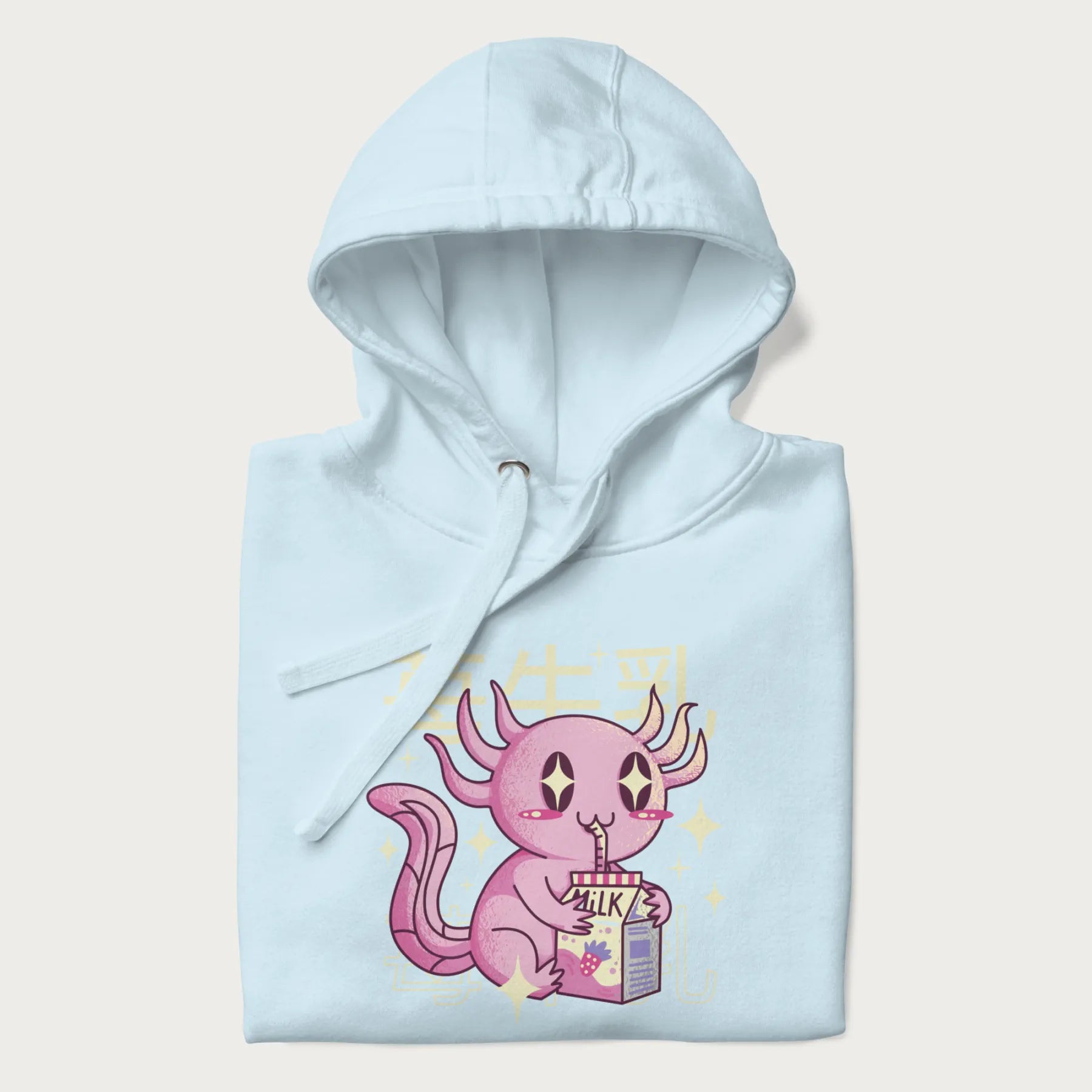 Folded light blue hoodie with Japanese graphic of a cute pink axolotl sipping strawberry milk from a carton, with Japanese text '苺牛乳' (Strawberry Milk).