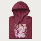 Folded maroon hoodie with Japanese graphic of a cute pink axolotl sipping strawberry milk from a carton, with Japanese text '苺牛乳' (Strawberry Milk).