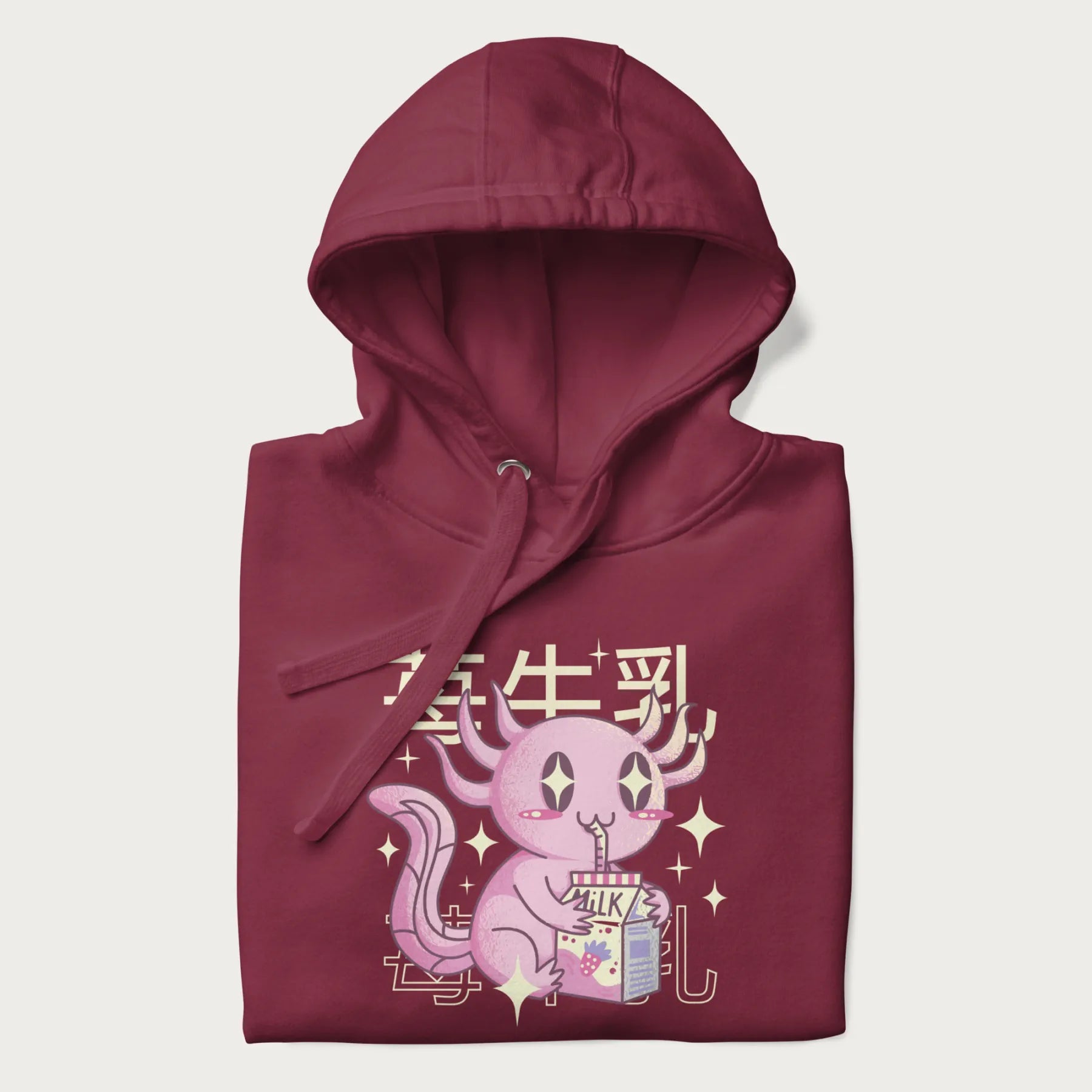 Folded maroon hoodie with Japanese graphic of a cute pink axolotl sipping strawberry milk from a carton, with Japanese text '苺牛乳' (Strawberry Milk).