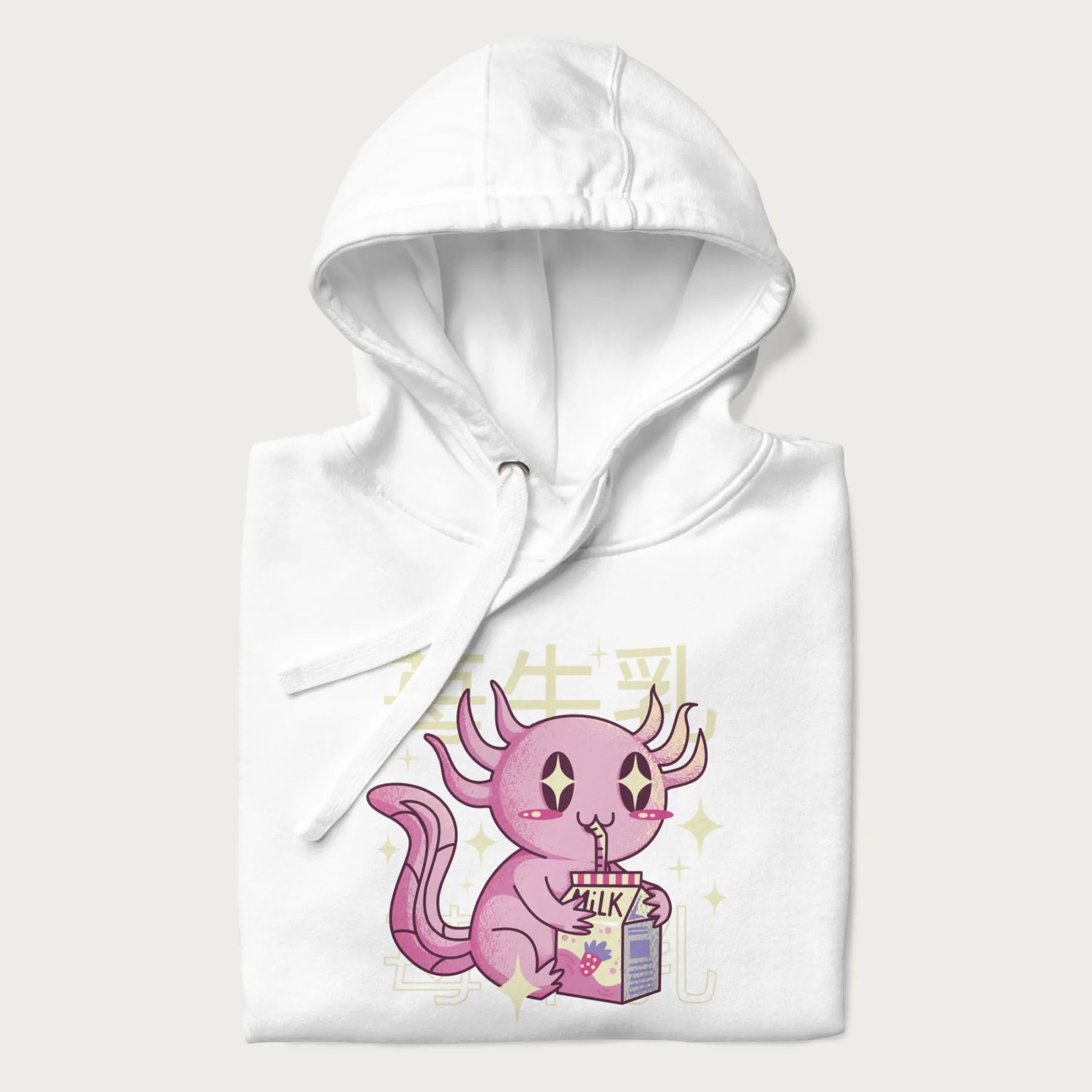 Folded white hoodie with Japanese graphic of a cute pink axolotl sipping strawberry milk from a carton, with Japanese text '苺牛乳' (Strawberry Milk).