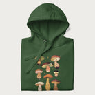 Folded forest green hoodie with Japanese graphic of cute and expressive mushrooms with various faces.