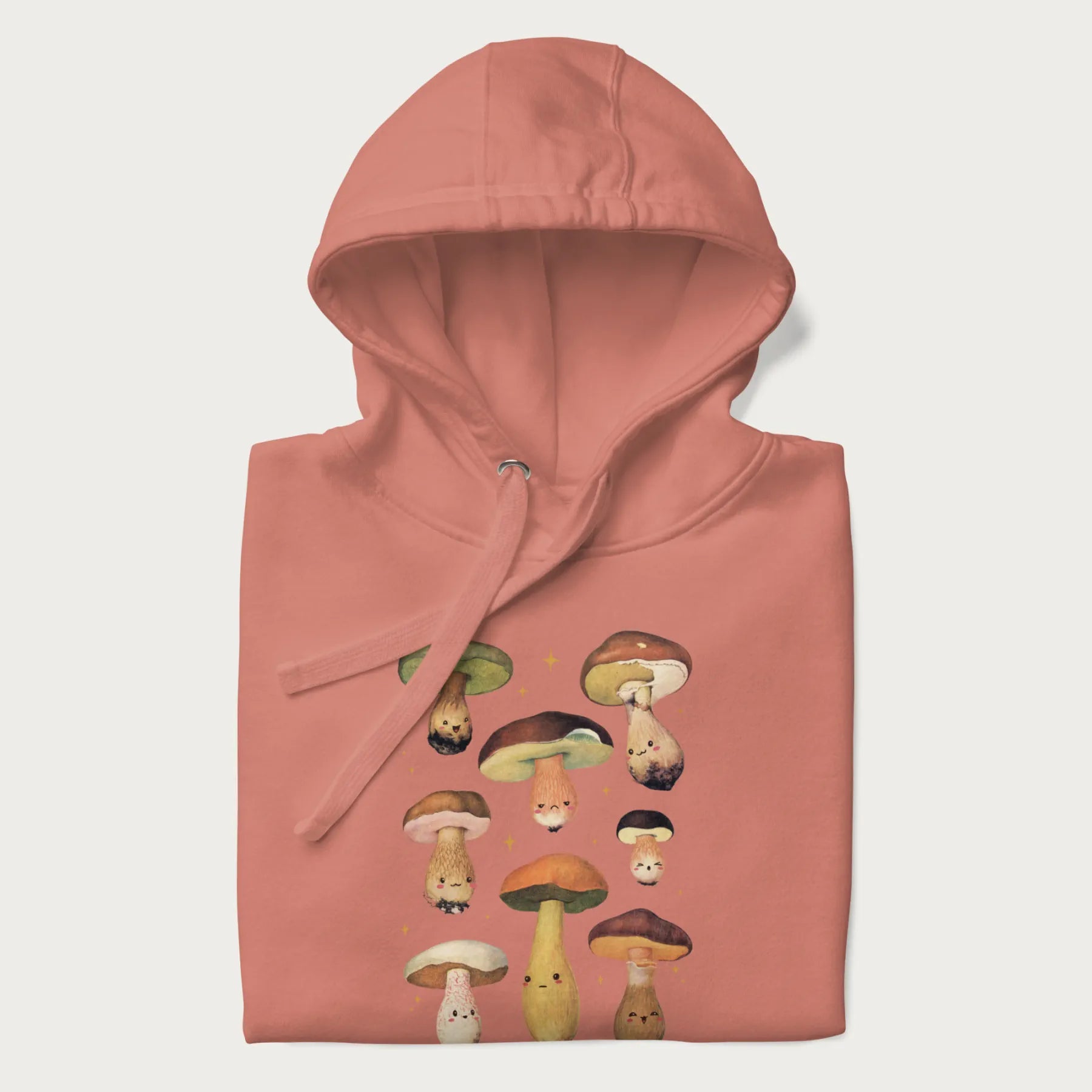 Folded light pink hoodie with Japanese graphic of cute and expressive mushrooms with various faces.