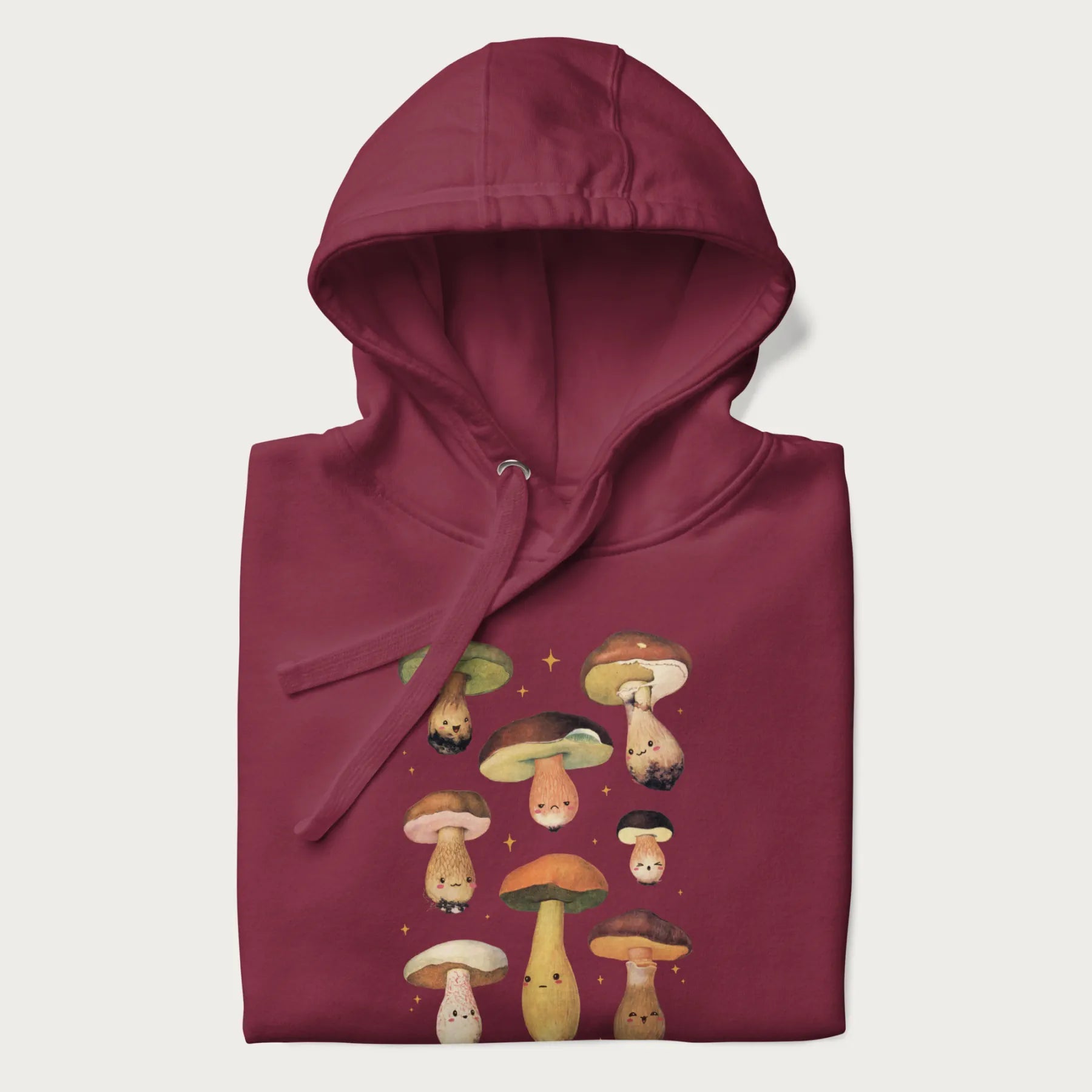 Folded maroon hoodie with Japanese graphic of cute and expressive mushrooms with various faces.