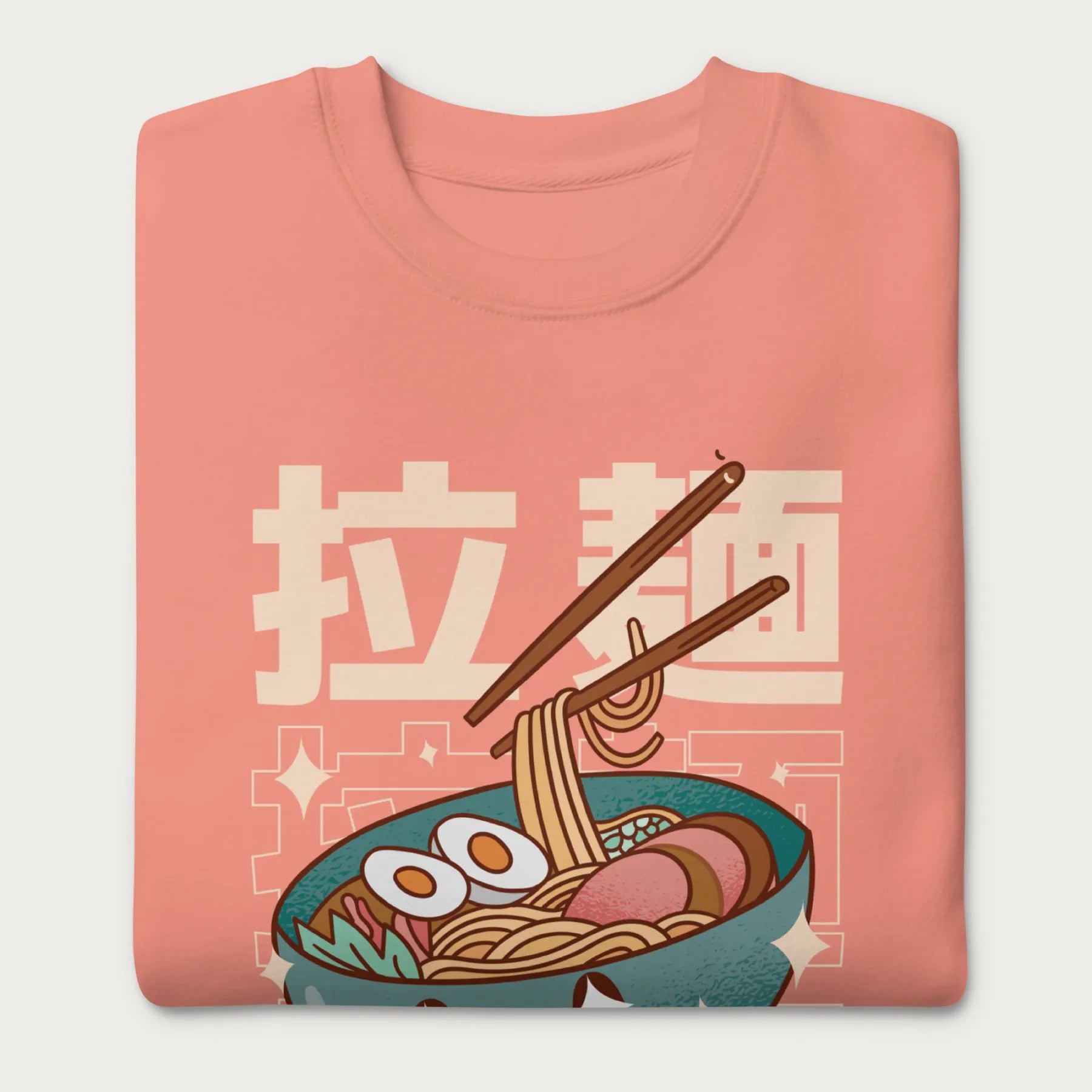 Folded light pink sweatshirt with Japanese text and a kawaii ramen bowl graphic.