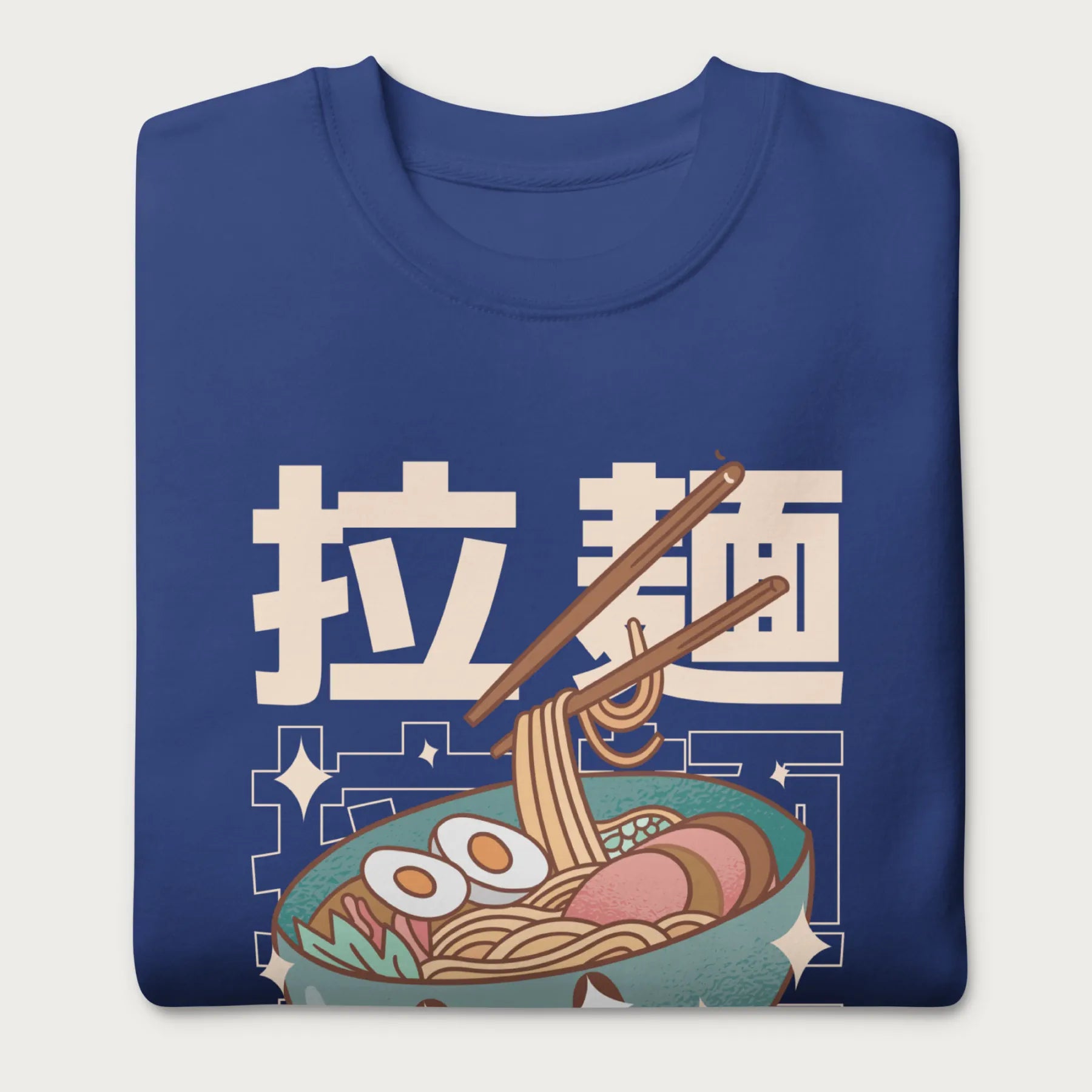 Folded royal blue sweatshirt with Japanese text and a kawaii ramen bowl graphic.