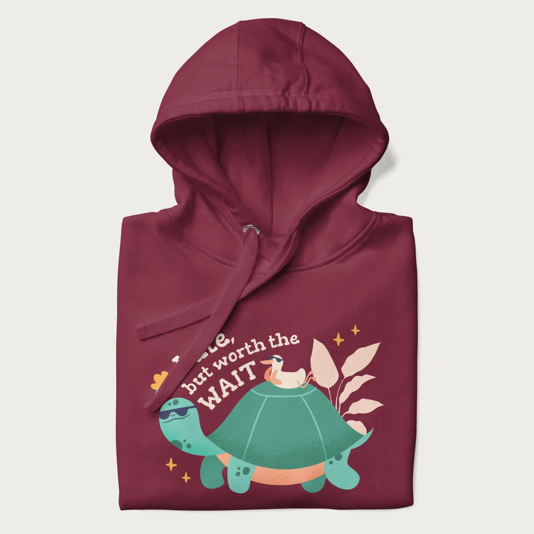 Folded maroon hoodie with graphic of a turtle and duck with sunglasses and the text 'Late but Worth the Wait'.