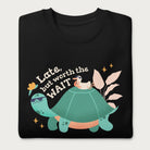 Folded black sweatshirt with a graphic of a turtle and bird wearing sunglasses with the phrase 'Late But Worth the Wait.'