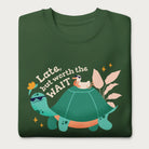 Folded forest green sweatshirt with a graphic of a turtle and bird wearing sunglasses with the phrase 'Late But Worth the Wait.'