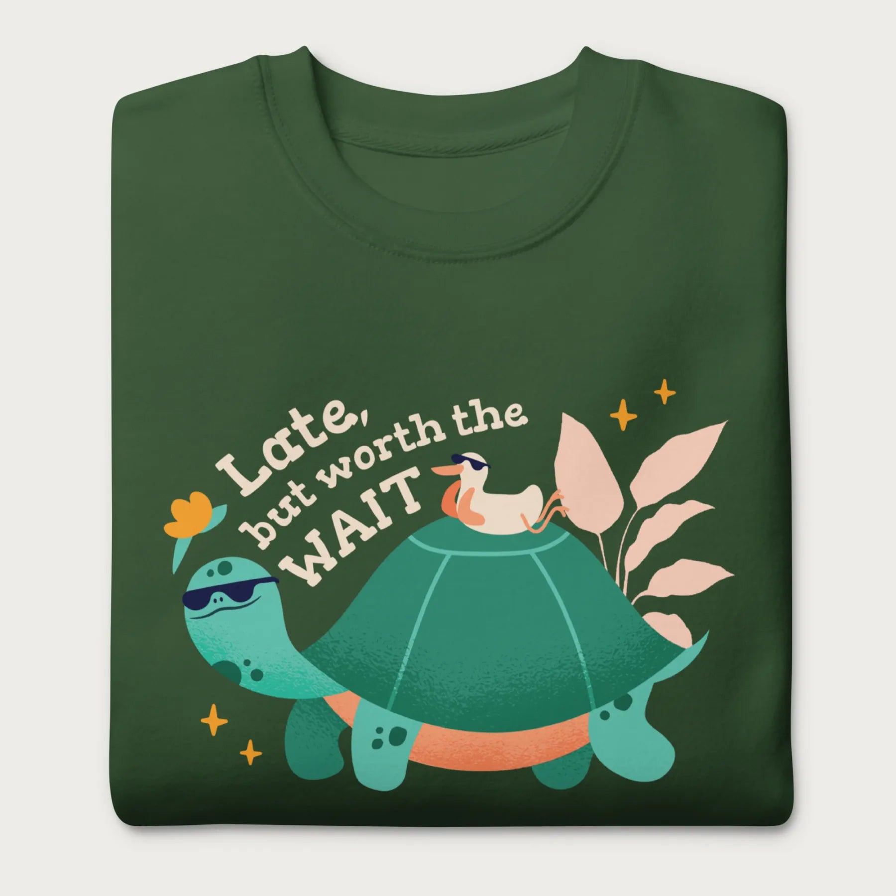 Folded forest green sweatshirt with a graphic of a turtle and bird wearing sunglasses with the phrase 'Late But Worth the Wait.'