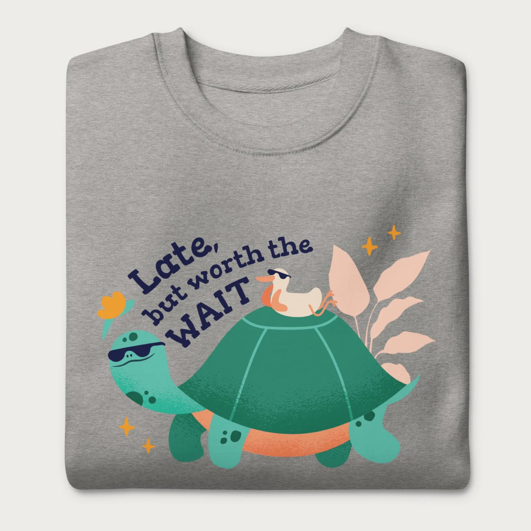 Folded light grey sweatshirt with a graphic of a turtle and bird wearing sunglasses with the phrase 'Late But Worth the Wait.'