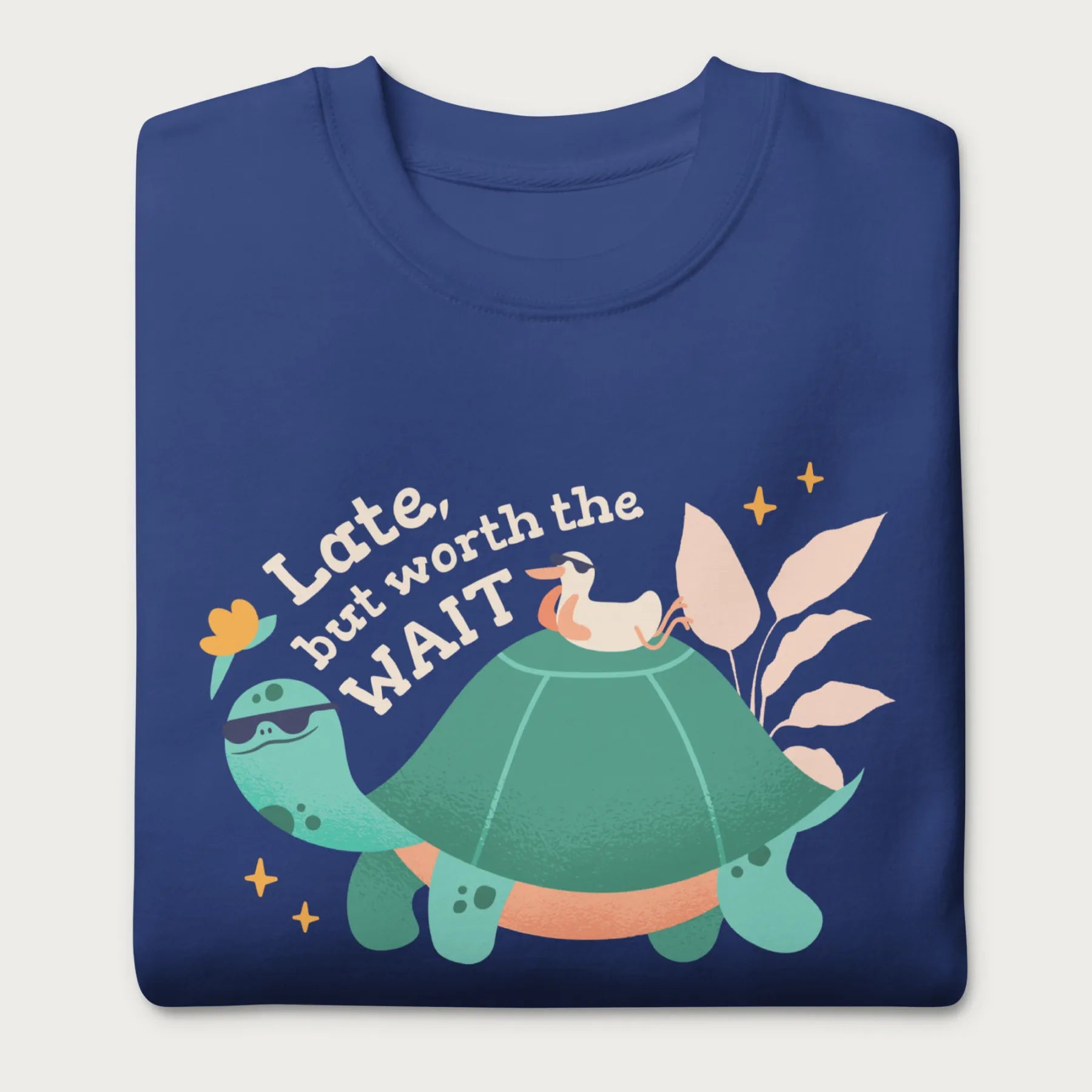 Folded royal blue sweatshirt with a graphic of a turtle and bird wearing sunglasses with the phrase 'Late But Worth the Wait.'