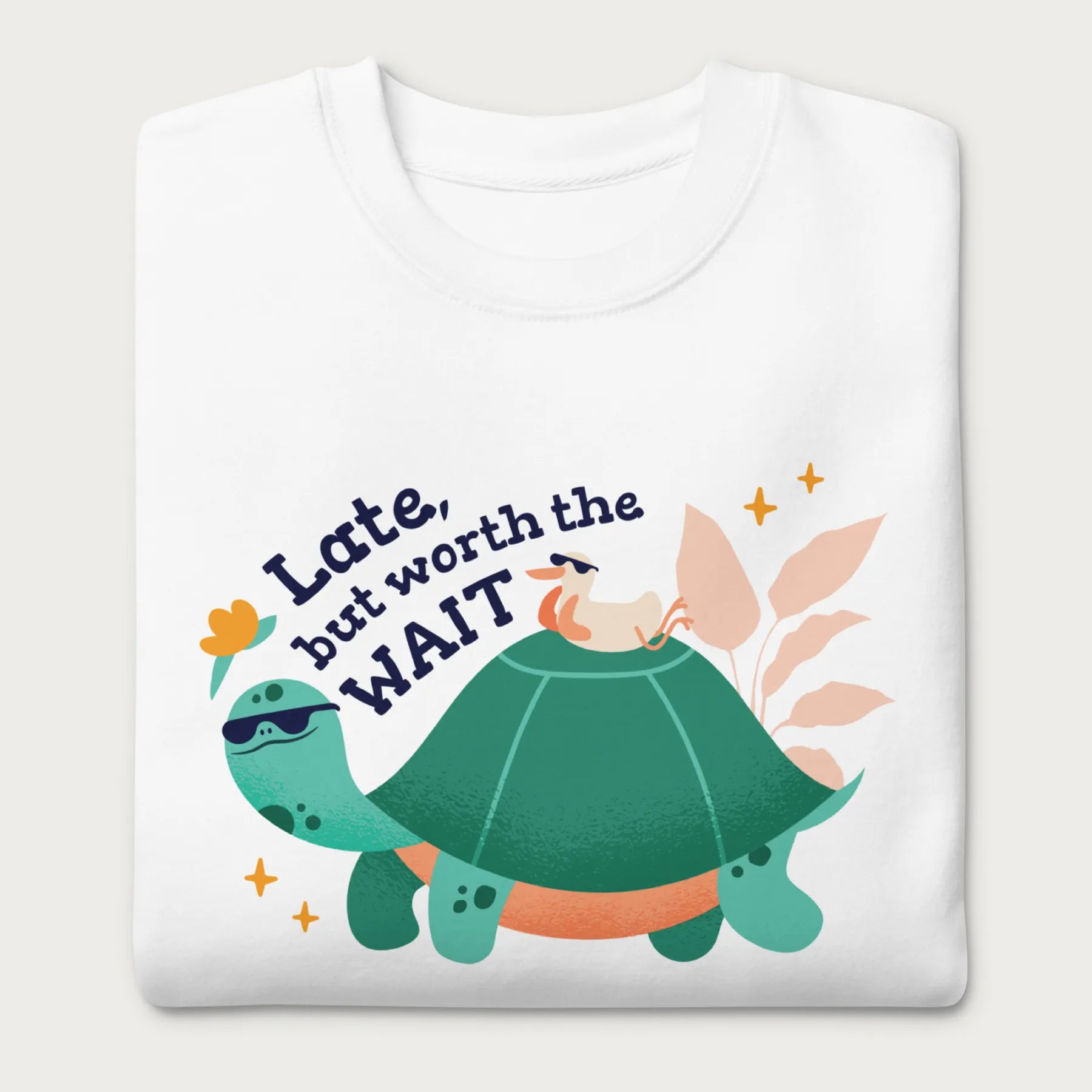 Folded white sweatshirt with a graphic of a turtle and bird wearing sunglasses with the phrase 'Late But Worth the Wait.'