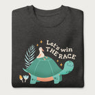 Folded dark grey sweatshirt with a graphic of a turtle with a bird on it's shell with the phrase 'Let's Win the Race.'