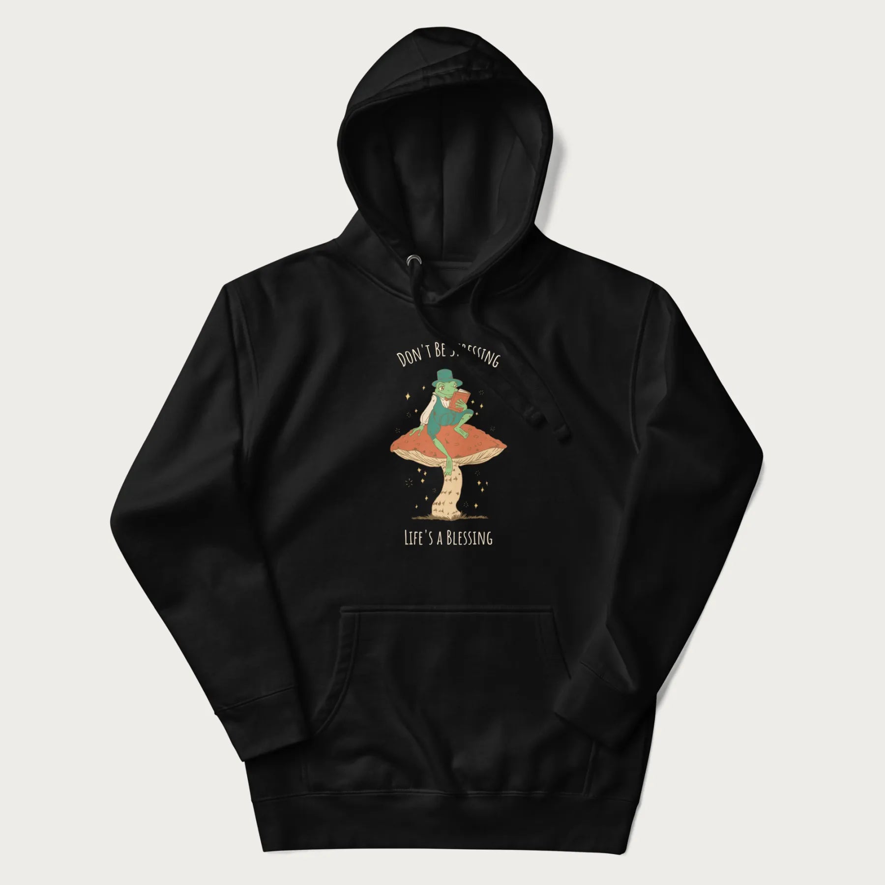 Black hoodie with graphic of a dapper frog reading a book on a mushroom with the text 'Don't Be Stressing, Life's a Blessing' above and below.