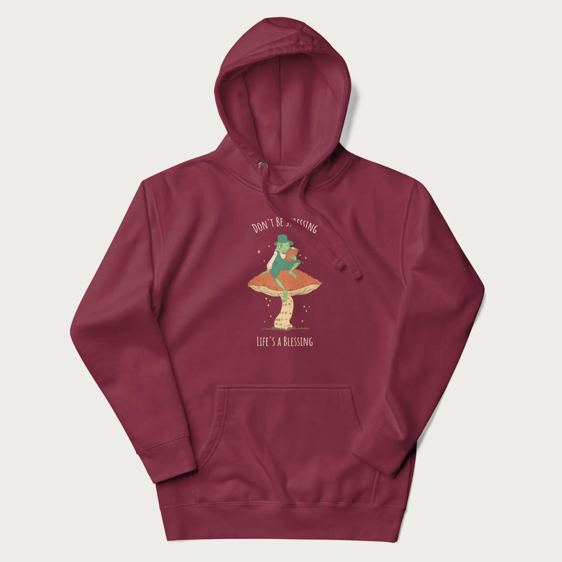 Maroon hoodie with graphic of a dapper frog reading a book on a mushroom with the text 'Don't Be Stressing, Life's a Blessing' above and below.