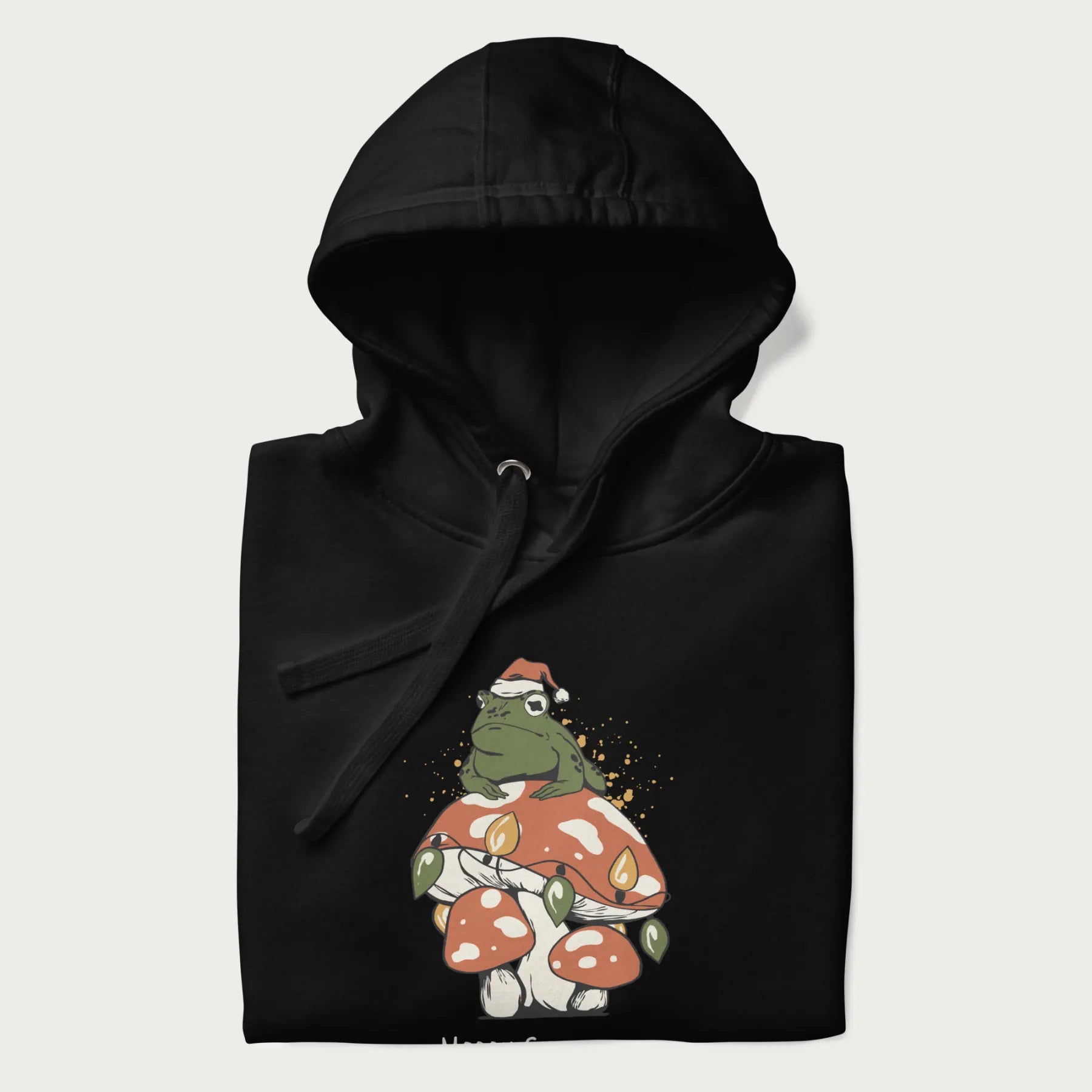 Folded black hoodie with graphic of a frog in a Santa hat on a mushroom with Christmas lights and the text 'Merry Christmas' below.