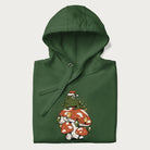 Folded forest green hoodie with graphic of a frog in a Santa hat on a mushroom with Christmas lights and the text 'Merry Christmas' below.