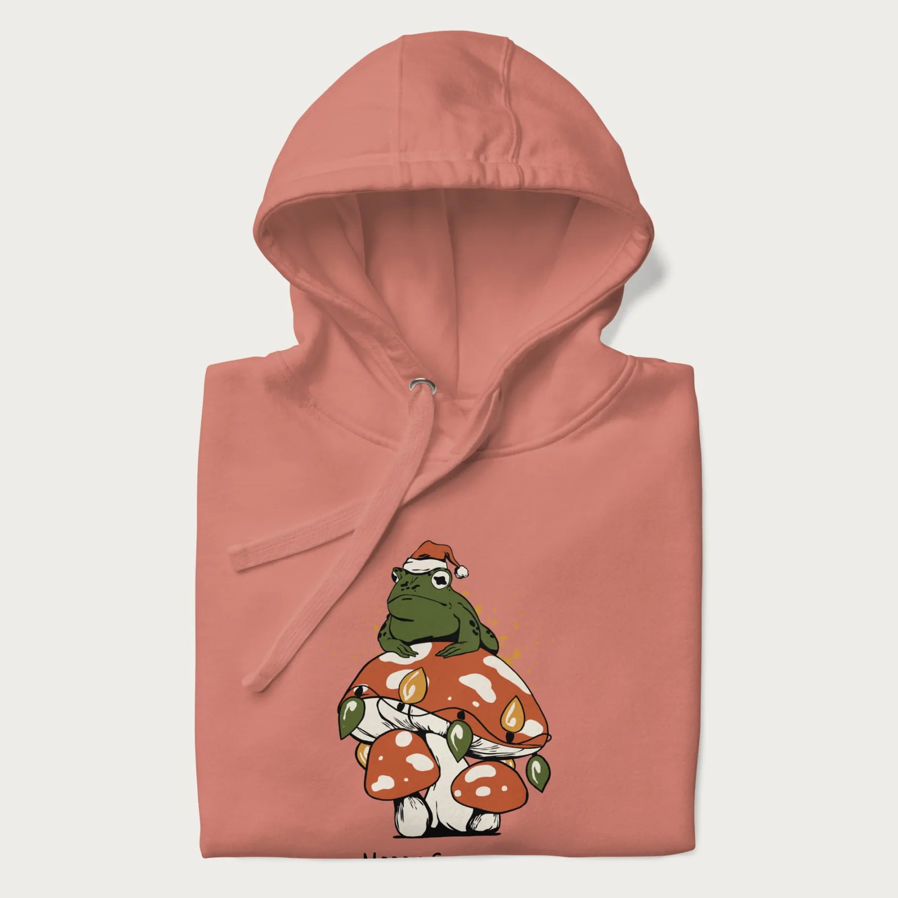 Folded light pink hoodie with graphic of a frog in a Santa hat on a mushroom with Christmas lights and the text 'Merry Christmas' below.