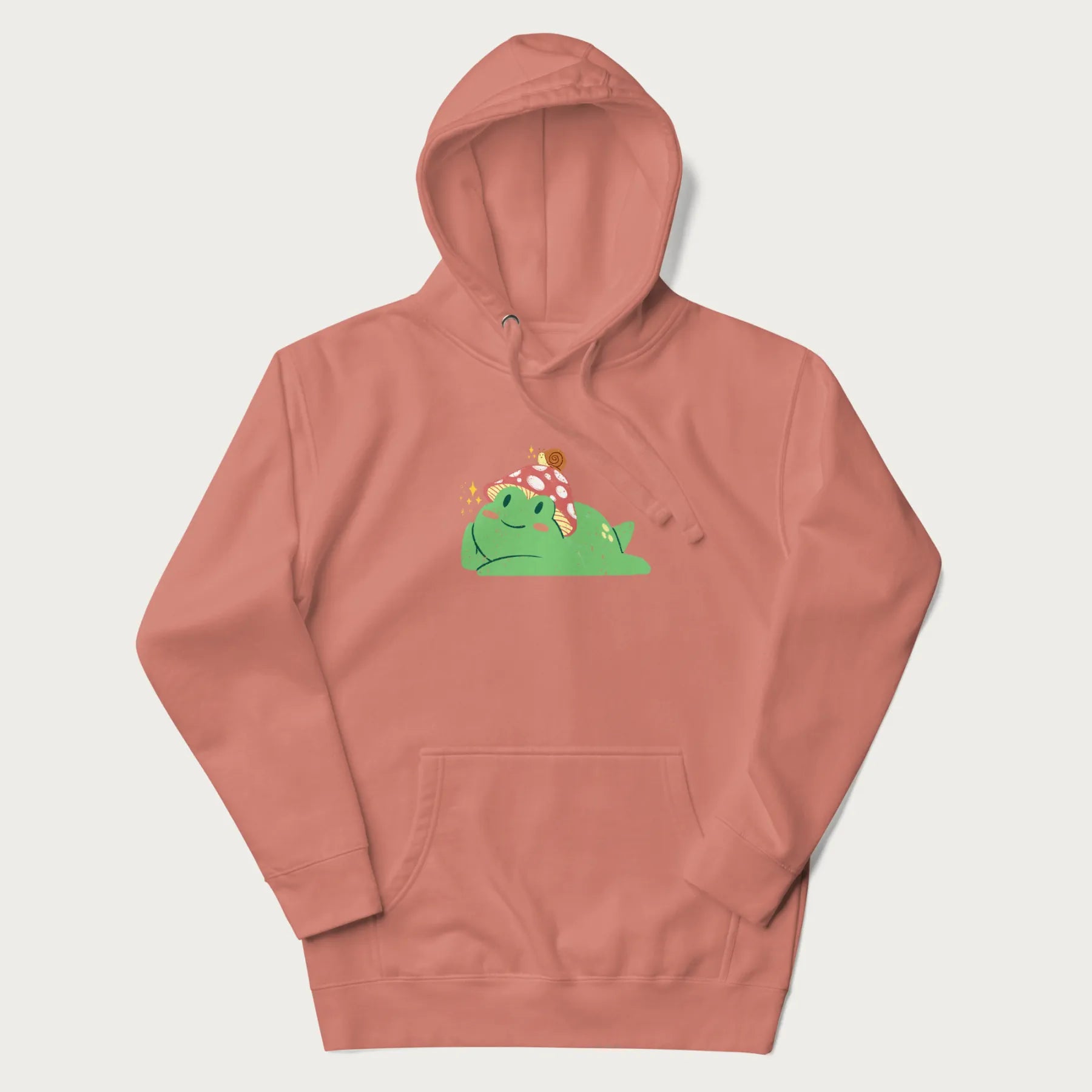 Light pink hoodie with a cottagecore design of a green frog wearing a mushroom cap and a snail on top.