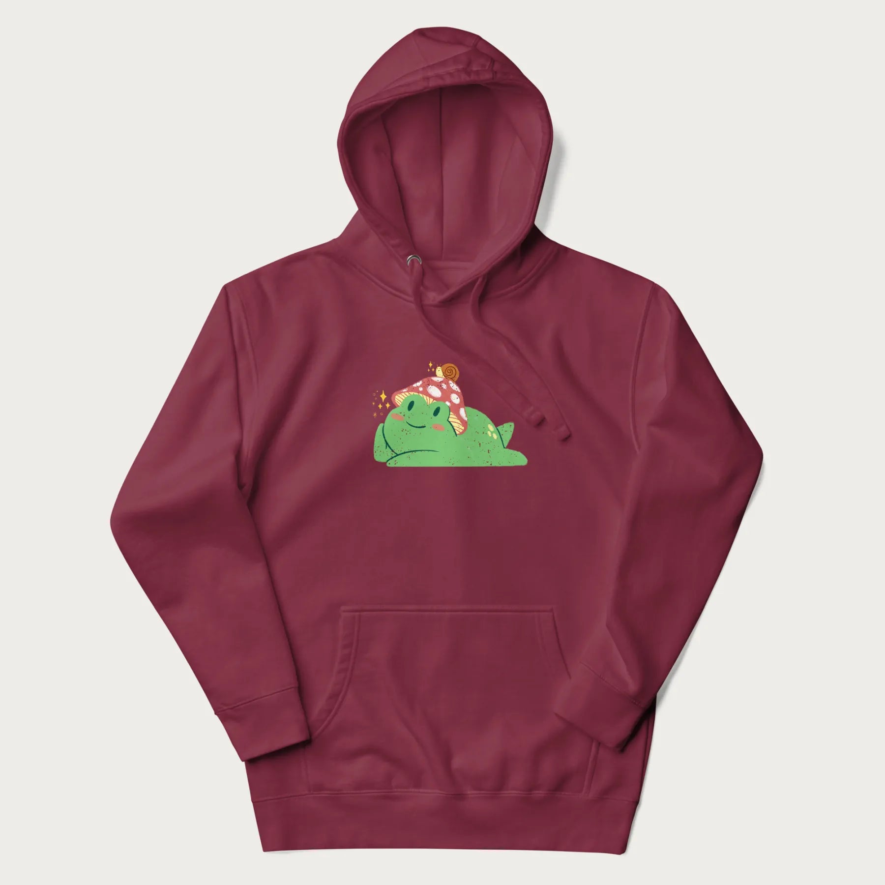 Maroon hoodie with a cottagecore design of a green frog wearing a mushroom cap and a snail on top.
