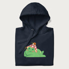 Folded navy blue hoodie with a cottagecore design of a green frog wearing a mushroom cap and a snail on top.