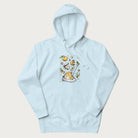 Light blue hoodie featuring a Cottagecore-themed graphic with oranges, a floral porcelain cup, orange pie, and daisies.