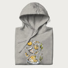 Folded light grey hoodie featuring a Cottagecore-themed graphic with oranges, a floral porcelain cup, orange pie, and daisies.