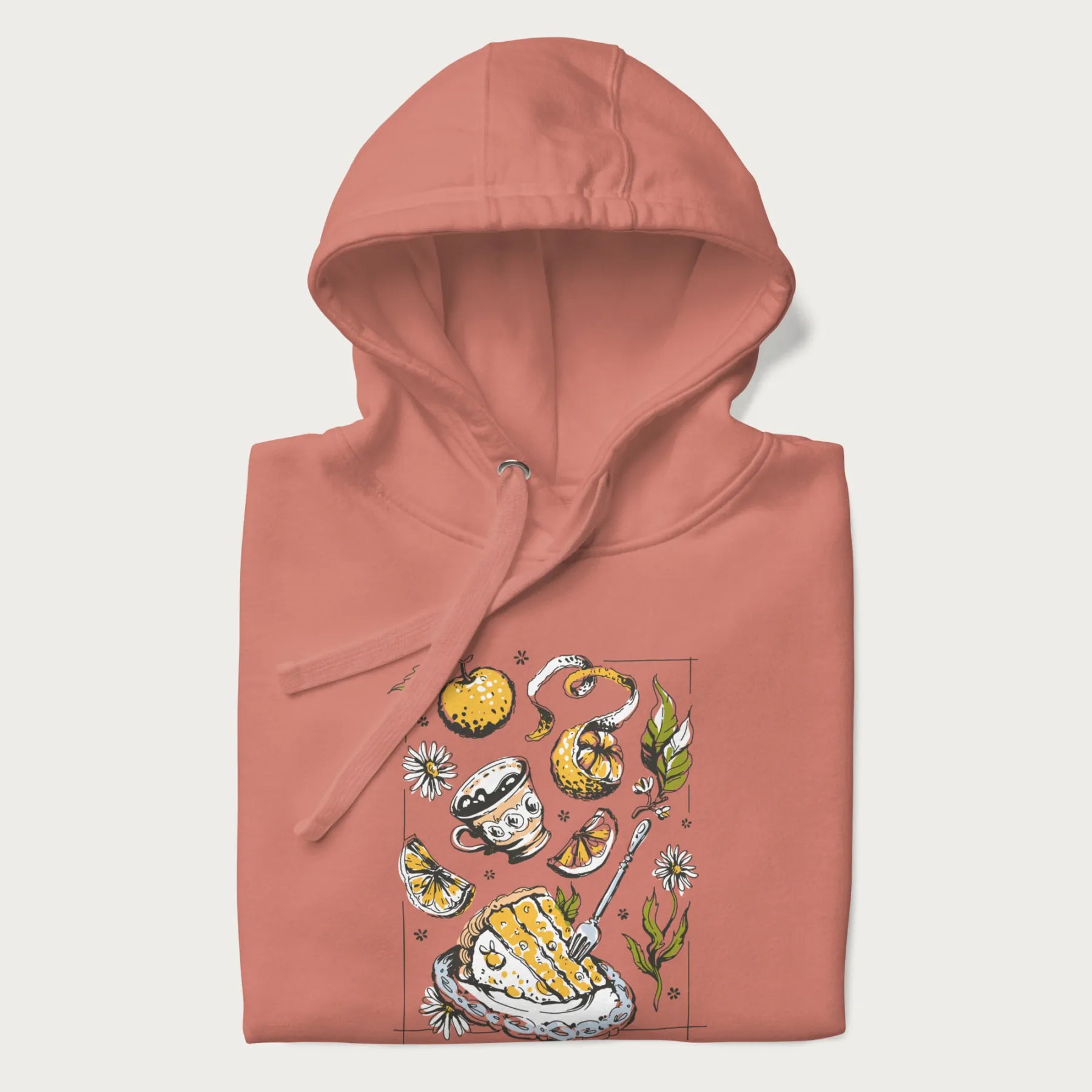 Folded light pink hoodie featuring a Cottagecore-themed graphic with oranges, a floral porcelain cup, orange pie, and daisies.