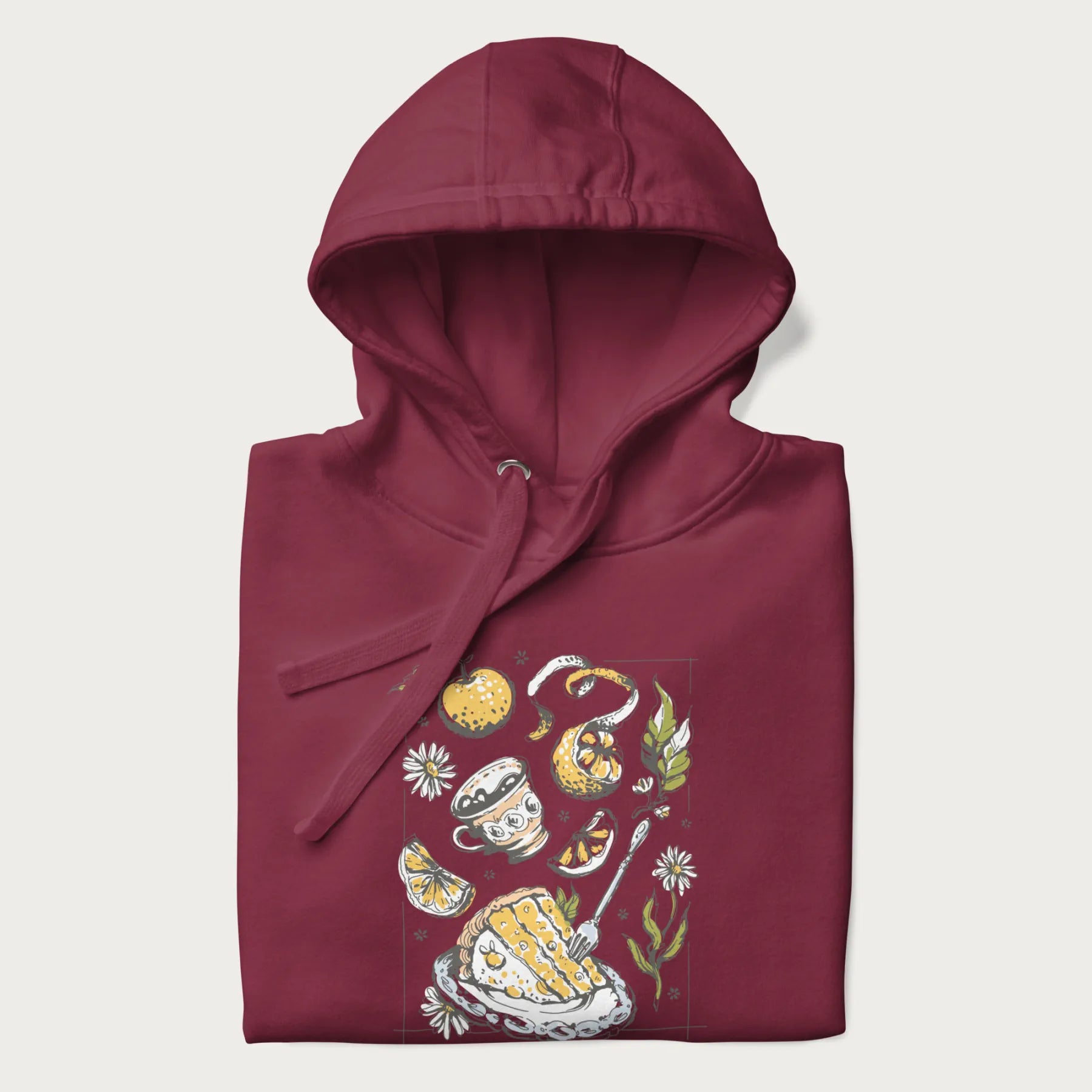 Folded maroon hoodie featuring a Cottagecore-themed graphic with oranges, a floral porcelain cup, orange pie, and daisies.