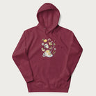 Maroon hoodie featuring a Cottagecore-themed graphic with oranges, a floral porcelain cup, orange pie, and daisies.