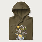 Folded military green hoodie featuring a Cottagecore-themed graphic with oranges, a floral porcelain cup, orange pie, and daisies.