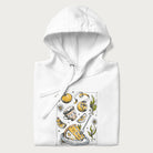 Folded white hoodie featuring a Cottagecore-themed graphic with oranges, a floral porcelain cup, orange pie, and daisies.