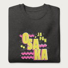 Folded dark grey sweatshirt with a vibrant graphic of the words "OSAKA JAPAN" in large yellow letters, surrounded by pink zigzag lines.