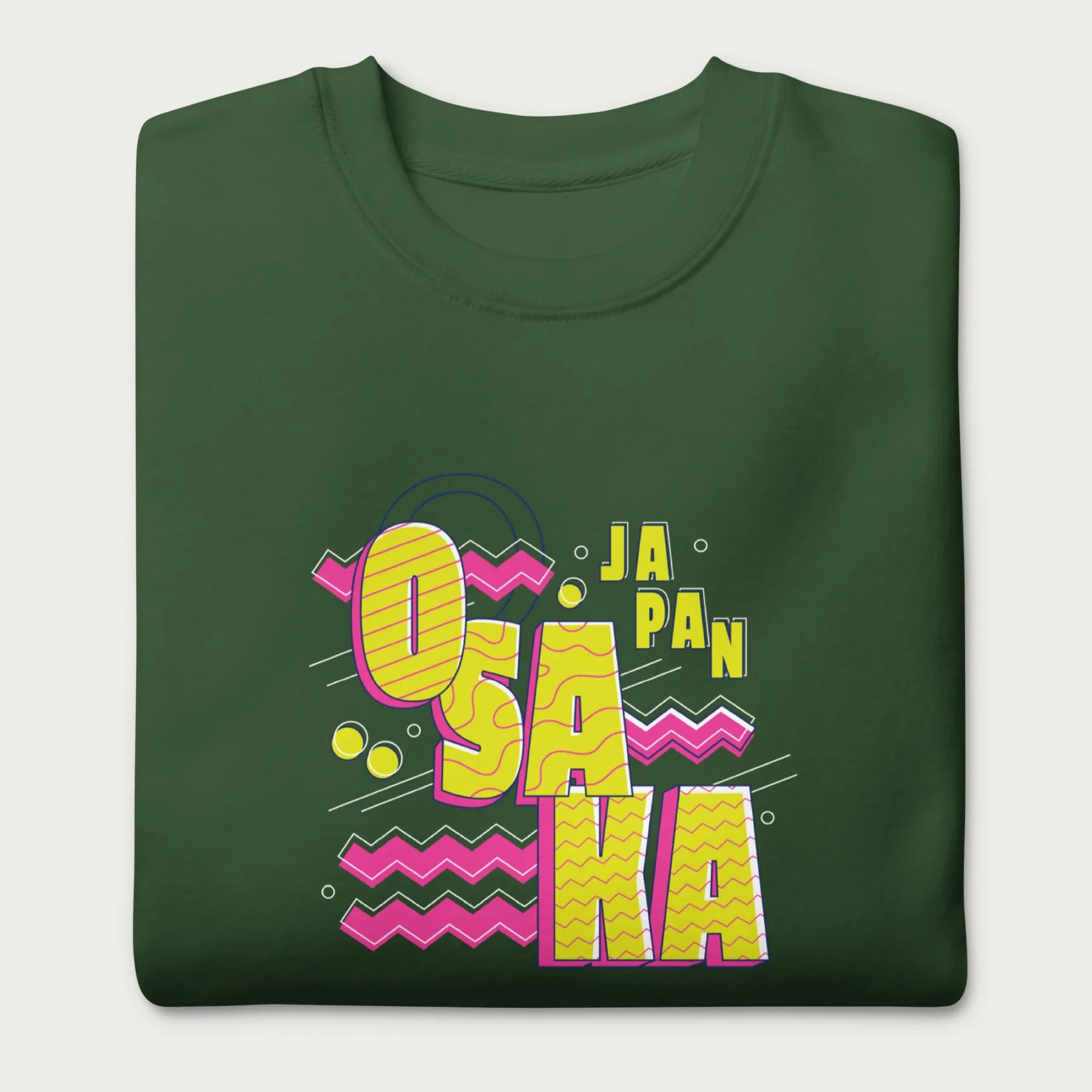 Folded forest green sweatshirt with a vibrant graphic of the words "OSAKA JAPAN" in large yellow letters, surrounded by pink zigzag lines.