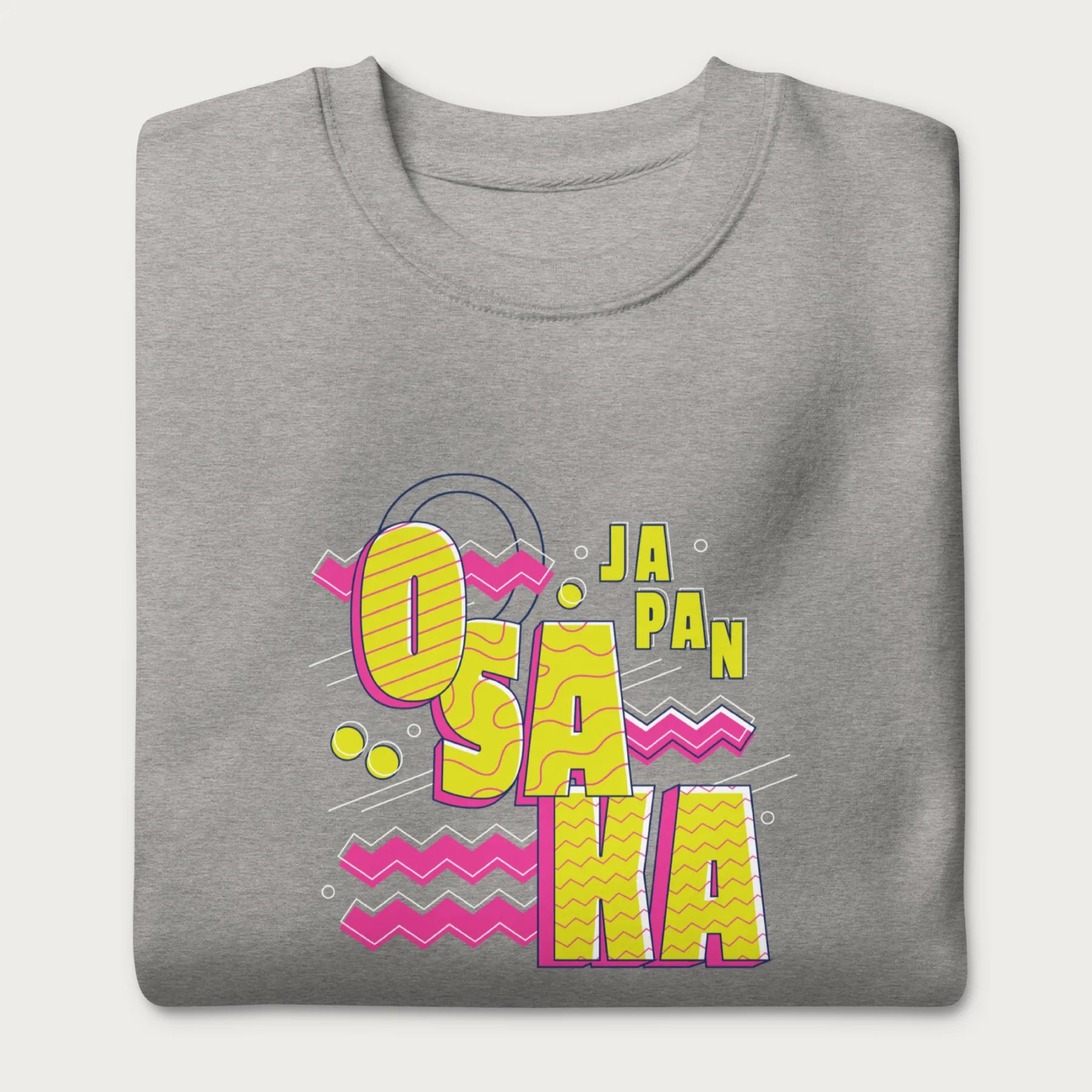 Folded light grey sweatshirt with a vibrant graphic of the words "OSAKA JAPAN" in large yellow letters, surrounded by pink zigzag lines.